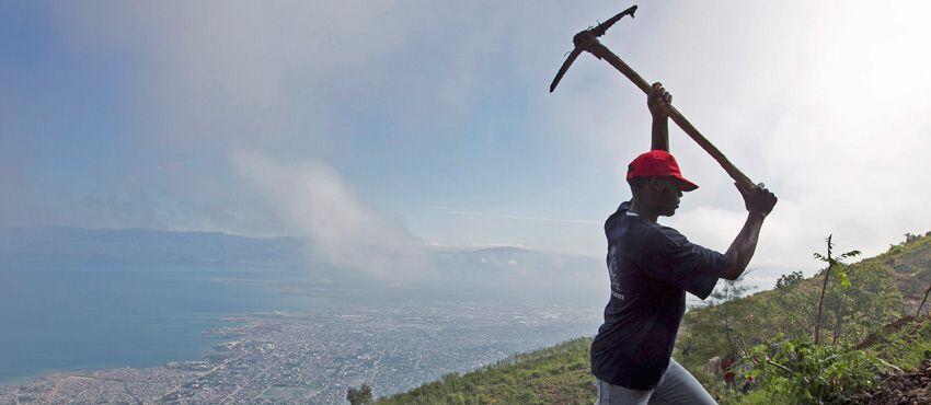 A worker in Haiti digs a hole for planting vegetation. 